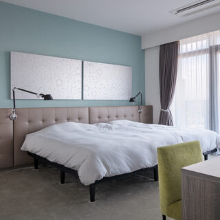 寝室はホテルライクなカーペットで。銀色のアートに合うように、壁はセージグリーン、ヘッドボードはグレージュとし、寒色と暖色でバランスをとりくすみカラーで統一した。