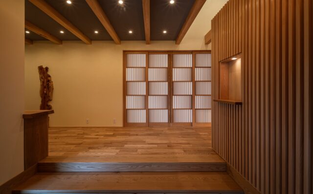 広くゆとりのある玄関ホール。主に来客用として使用される。右側の上部は吹き抜けで、明るく空間の広さを感じる。堂々とした玄関から続く場所として、違和感がない空間を意識した。右側の格子壁の奥には、家族用の玄関とシューズクローク。正面に見える造作の飾り障子が美しい