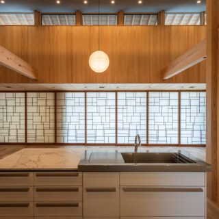 キッチン奥から見た庭方向。左右の壁の質感の違いと造作の飾り障子の美しさを楽しむことができる。障子の模様は、右側にある十和田石の壁と調和するデザインとした。全体的に木材に囲われ、安らぎと安心感を感じる