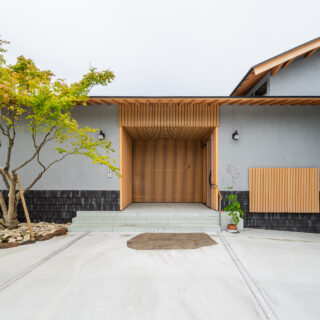 「堂々とした玄関を」というお施主様の要望に答えた、木材を多用した玄関。堂々としているが、威圧感なく美しい場所を追求した。外壁は周囲に威圧感を与えずに調和する、落ち着いた色を採用