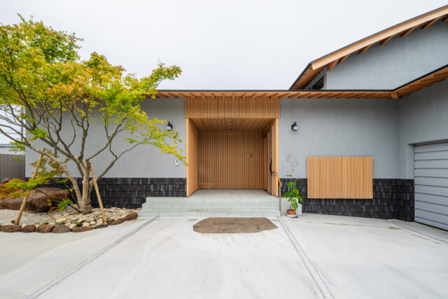 「堂々とした玄関を」というお施主様の要望に答えた、木材を多用した玄関。堂々としているが、威圧感なく美しい場所を追求した。外壁は周囲に威圧感を与えずに調和する、落ち着いた色を採用