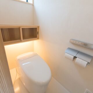 間接照明の柔らかな陰影が奥行きをもたらすトイレ。造作の収納棚にはすりガラス入りの扉がつけてあり、生活感が出やすいトイレ周りのアイテムを目隠ししてくれる