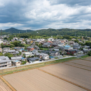 上空から。中央にあるL字型の平屋が本作品。眼前にすばらしい田園が広がる一方、背後の高台に家屋が密集している周辺環境がよくわかる。こうした特徴をすべて活かしたのがこの作品だ。近隣に溶け込む外観にも好感が持てる