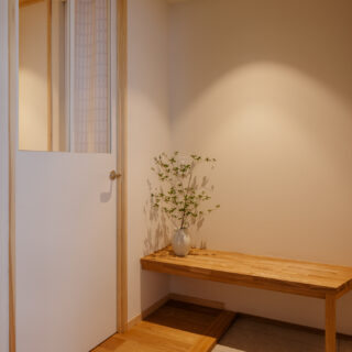 以前より面積を拡大し柔らかく温もりある玄関に。片隅には、木製ベンチを配置。ちょっとした荷物置きや靴の脱ぎ履きに重宝する。