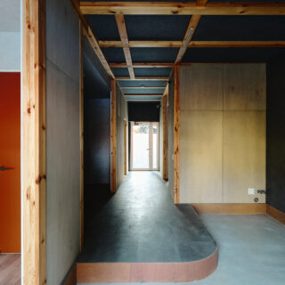 山棟の住戸。店舗スペースから奥のインナーバルコニーへ通り土間が伸びる。内装は現しの柱などで木の温かみをプラス。空間の用途で色のトーンを変えており、通り土間などのパブリックゾーンは少し暗めの落ち着いた色使い。正面の窓越しに見える光や緑とのコントラストが際立つ