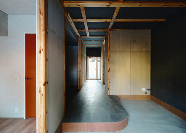 山棟の住戸。店舗スペースから奥のインナーバルコニーへ通り土間が伸びる。内装は現しの柱などで木の温かみをプラス。空間の用途で色のトーンを変えており、通り土間などのパブリックゾーンは少し暗めの落ち着いた色使い。正面の窓越しに見える光や緑とのコントラストが際立つ