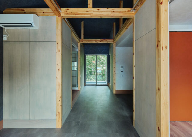 庭棟の住戸。玄関を入るとシックな通り土間の先に明るい緑が見え、思わず笑顔になってしまう。キッチンと個室を仕切る建具は（写真右）、緑と引き立て合う赤をセレクト。どの住戸も、差し色としてところどころに赤を入れている