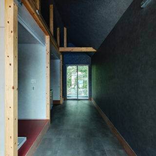 森棟の住戸。奥の窓越しに森の緑が見える。通り土間の床はフロアタイル、天井と壁のクロスは同系色だが質感を変えており、天井はざらっとした風合いのものを使用。一方、壁のクロスは光沢のあるタイプで、陽光と共に森の緑が映り込んで美しい