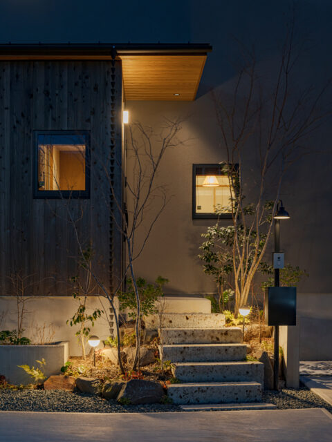 暖色の柔らかな光が、木の質感と植栽を静かに浮かび上がらせる。夜の足元を優しく守りながら、住まいを穏やかな表情で彩る空間演出。