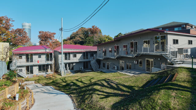 新横浜駅から徒歩11分。駅周辺のビル群を望む小高い住宅街に立つ「森庭山荘」。写真左奥から時計回りに、斜面下の森に面した森棟と庭棟、写真右が斜面の傾斜に沿って建てられた山棟。L字を成した3棟が庭を囲んだ配置となっている
