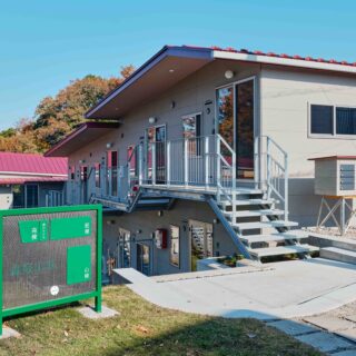 緑に映える赤い屋根、地形を生かした個性的なデザインが目を引く。敷地の入口では、3棟の配置を示す案内板が訪れた人をお出迎え。写真右、建物手前にある郵便受けはウミネコアーキでDIY。イームズチェアを思わせる脚は百葉箱用のもの。センスあふれる素材使いが楽しい