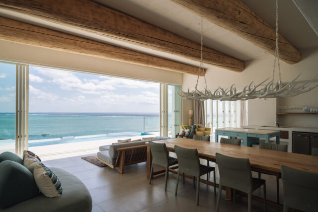 玄関ホールを抜けると、この景色がいきなり目に飛び込んでくる。「ゲストをもてなしたい」というオーナーの要望を見事に形にした粋な演出だ。天井に3本伸びるヒノキの丸太梁が唯一無二の雰囲気を醸す。ダイニングのエゾジカのシャンデリアも独特の雰囲気づくりに一役買っている