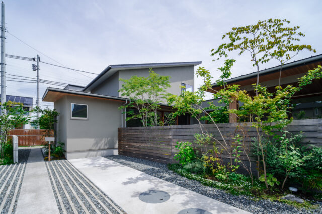 外壁は質感や耐候性に優れた塗装剤の左官塗り。中庭は木塀で覆いプライバシーを確保した。植栽は生活スペースが隠れるように、玄関（写真左奥）、庭の入口、庭の奥と、敷地の外側から奥に向かってバランス良く配置。人目を遮ると共に奥行きが強調され、空間の豊かさを感じられる