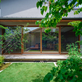 窓は温かみのある木製サッシを採用し、光や緑といった自然の要素と調和する美しい景観をつくり出している。写真は中庭からLDKを見たところ。大開口の窓によって邸内・テラス・中庭の一体感が高まり、屋外の爽やかな開放感を満喫できる