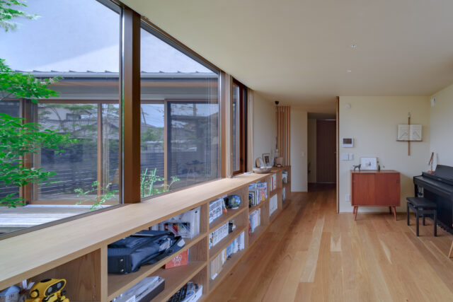 中庭を囲む空間の1つであるフリースペースは、お子さんのピアノやHさん所蔵のコミック本を置く場所が欲しいとの要望に応えてつくった。2階に子ども部屋はあるものの、お子さんたちはここで過ごすことが多いそう。中庭を挟んだはす向かいはLDKで、家族の距離感もほどよい