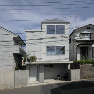 前面道路側に寄せた地階＋地上２階建て。南北に大小２つの棟が寄り添う構成で、斜線制限をクリア。道路と庭の高低差を解消するため、RC造の上に木造を載せる混構造を採用。擁壁一体の構造により、同じく混構造である写真左の実家との調和を実現。