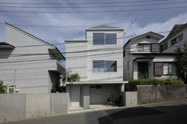 前面道路側に寄せた地階＋地上２階建て。南北に大小２つの棟が寄り添う構成で、斜線制限をクリア。道路と庭の高低差を解消するため、RC造の上に木造を載せる混構造を採用。擁壁一体の構造により、同じく混構造である写真左の実家との調和を実現。