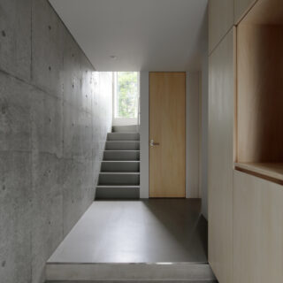 RC造のコンクリート打ち放しの玄関。地階には寝室と洗面室・浴室といった水回りを配置。階段の先にあるのが、庭へ向かう第二の出入り口。ガラス扉にしたことで、庭からの光が降りてくる。