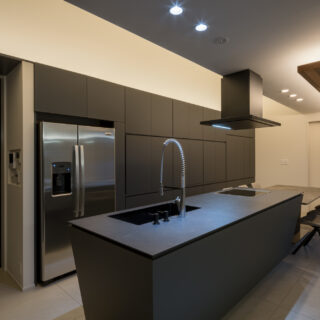 天井高を低くしたキッチンはブラックで統一されたシックな装い。堺さんが設計した収納棚は、使用時に開いた扉が邪魔にならないよう収納できるよう（垂直収納扉）になっているという。