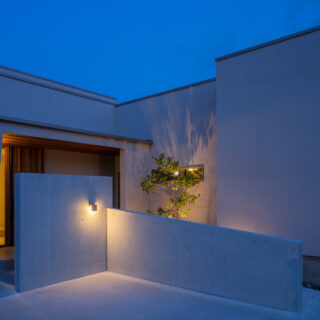道路から玄関が丸見えにならないようコンクリートの壁で目隠し。ライトアップされた木の陰がシックな雰囲気を醸し出している。