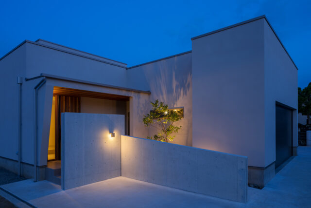 道路から玄関が丸見えにならないようコンクリートの壁で目隠し。ライトアップされた木の陰がシックな雰囲気を醸し出している。