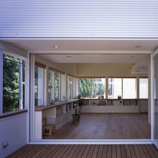 テラスからリビング方向を見ると、2面の窓越しに並木を遠くまで見ることができる。折れ戸の高さは2.2ｍ。既製品の高さに天井高を合わせることで、コストを削減した。テラスは北側に配置。室内の収納と高さを合わせた腰壁で囲むことで、開放感とプライバシー確保を両立させている
撮影：石黒 守