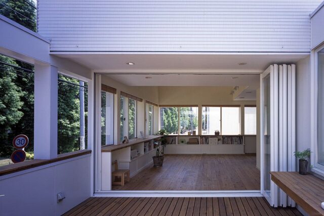 テラスからリビング方向を見ると、2面の窓越しに並木を遠くまで見ることができる。折れ戸の高さは2.2ｍ。既製品の高さに天井高を合わせることで、コストを削減した。テラスは北側に配置。室内の収納と高さを合わせた腰壁で囲むことで、開放感とプライバシー確保を両立させている
撮影：石黒 守