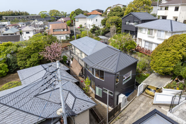 画像中央、黒い外壁の建物が「鎌倉山の住宅Ⅱ」。奥に続く白い外壁の家は息子さま家族が暮らす既存建物。高台にあり家に囲まれている立地から多くの法的制限がかかるため様々な困難が予想され、当初は依頼を請けるハウスメーカーや施工会社が見つからなかった