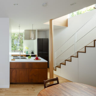 1階ダイニングからキッチン方向を見る。画像左に玄関への扉が見える。キッチンの奥にも玄関への扉を計画し、回遊性を持たせた。奥さまは玄関からキッチンを通り階段へアクセスできる。階段下は収納。介護用品など、散らかりやすいものをさっと仕舞えて便利