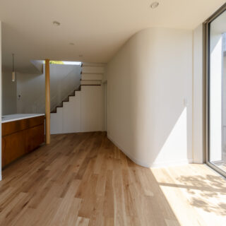 1階。車椅子を使用するため、床は傷に強い塗装を施した素材を採用。巾木もやや高めに設定し、壁の汚れを防ぐ。右の壁面は一部アールに。光が柔らかく室内に広がり、自然と屋外へ視線が伸びる。壁面の裏は水回り。あえて南側に配置し、明るく快適な水回り空間を実現