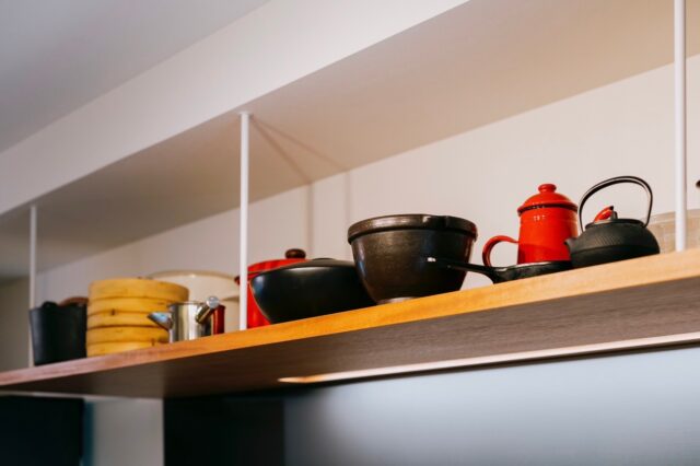 キッチンのオープン吊戸棚。見せる収納だけでなく、サイズが大きい鍋なども収納できる利点がある。棚の木はキッチンと同じもの。多くの素材を使わず、統一感とシンプルさを追求した