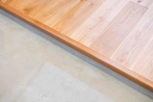 玄関のたたきとフローリング。段差を抑え、上がり框は細くすることでシンプルさを追求した。オーク材無垢の2ｍｍ厚節付きフローリングを採用。価格を抑えられるだけでなく傷や汚れが目立たないメリットもある。下地は遮音性能LL-45相当の二重床で下階に配慮した