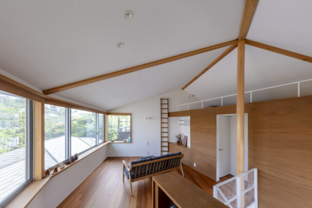 2階、書斎からリビング、ロフトを見る。切妻屋根側のリビングは天井が高く開放的。一面を大開口した南側には鎌倉山の景色が広がり贅沢だ。木板が貼られた右側の箱の中は寝室とトイレ。リビング側に収納を計画し、寝室内の壁が直角になるよう計画。場にふさわしい落ち着きを実現