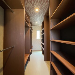 棚やハンガーラックが並ぶ大容量のWIC。天井には高級感ある壁紙を採用した。