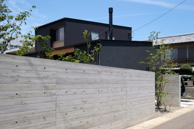 外観。周囲と馴染むことを期待し、外構のコンクリートには無垢の杉板を型枠として使用した。実際に板を張ったことにより表情がさまざまで、コンクリートでありながら有機的な雰囲気がある。住宅街にあるため、庭の中の様子は外からは見えないようにした
