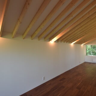 2階、洋室2。2階は切妻屋根を反映した天井が居心地のバリエーションをふやしている。この居室では楽器演奏やミシンなど趣味を楽しまれる予定。使う電化製品や電子機器も多いだろうと、コンセントは豊富に設置した。画像右奥の壁面にはパネルヒーターを設置した