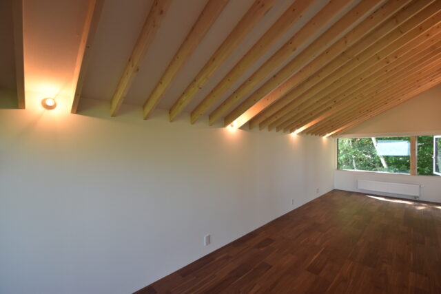 2階、洋室2。2階は切妻屋根を反映した天井が居心地のバリエーションをふやしている。この居室では楽器演奏やミシンなど趣味を楽しまれる予定。使う電化製品や電子機器も多いだろうと、コンセントは豊富に設置した。画像右奥の壁面にはパネルヒーターを設置した