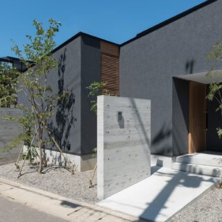 外観。画像右が玄関ポーチ。左の外構裏に庭がある。中央に見えるルーバーは建具で、中の通路を通り庭と行き来ができるよう計画。また、光や風も通す役目も担っている。掃除用具などをしまうテラスと繋がり、利便性の高さと安全性を両立した