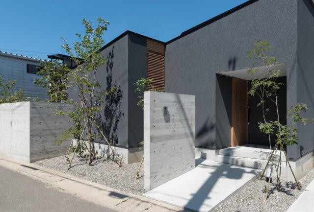 外観。画像右が玄関ポーチ。左の外構裏に庭がある。中央に見えるルーバーは建具で、中の通路を通り庭と行き来ができるよう計画。また、光や風も通す役目も担っている。掃除用具などをしまうテラスと繋がり、利便性の高さと安全性を両立した