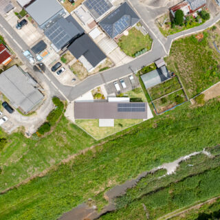 上空から。敷地を斜めに使った建物配置と、川の土手に面して視線がなく、落ち着いたプライベート空間となる庭の様子がよく分かる。２階建て部分を奥側にすることで周囲への圧迫感を減少させた。コスト対策で、シンプルな長方形となっていることもよくわかる