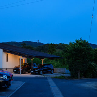 集落に入り、さらに進むとこの光景となる。周辺の住人もこの風景を見て帰宅するので、景観を邪魔しないように。片流れの奥に壁を設けず、山が見えるように配慮した。建物を敷地内で斜めにすることで、視線をずらして圧迫感を減少させる意図もある