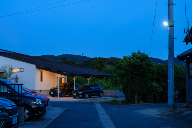 集落に入り、さらに進むとこの光景となる。周辺の住人もこの風景を見て帰宅するので、景観を邪魔しないように。片流れの奥に壁を設けず、山が見えるように配慮した。建物を敷地内で斜めにすることで、視線をずらして圧迫感を減少させる意図もある