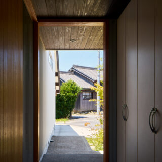 玄関から駐車場へ続く通路。右は収納スペース、左に玄関扉。近隣の風景を切り取るフレーミングを意図した