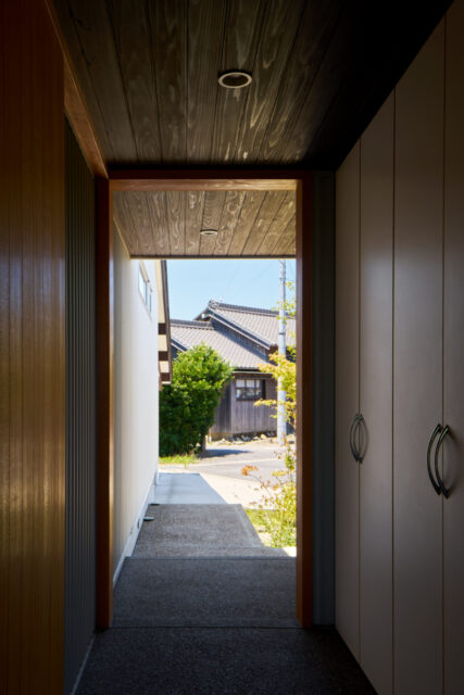 玄関から駐車場へ続く通路。右は収納スペース、左に玄関扉。近隣の風景を切り取るフレーミングを意図した
