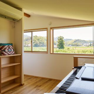 2階に配されたフリールーム。この窓から見える山々が、お施主様の奥様が幼い頃に見ていた景色だ。大のお気に入りで、趣味のピアノを弾いたり、窓からの景色を楽しんでいるという。この家唯一のエアコン（左上）で、家全体の空調が可能だ