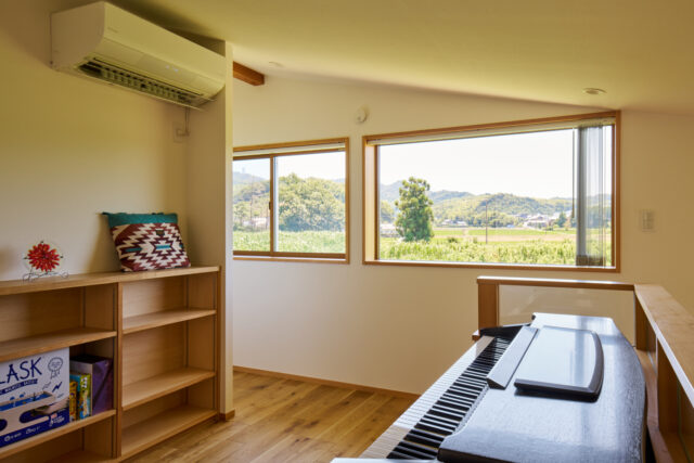2階に配されたフリールーム。この窓から見える山々が、お施主様の奥様が幼い頃に見ていた景色だ。大のお気に入りで、趣味のピアノを弾いたり、窓からの景色を楽しんでいるという。この家唯一のエアコン（左上）で、家全体の空調が可能だ