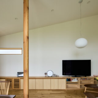 リビング。LDKは吹き抜けのため、屋根が高い側には巨大な壁が出現することとなる。その圧迫感を減らすために、壁の角（写真右）を曲線とすることで柔らかな印象を与える工夫がなされている。正面の壁は季節や時刻によって色が変わる。外の緑や太陽光の反射が美しい