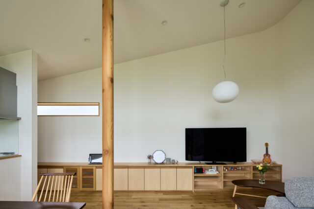 リビング。LDKは吹き抜けのため、屋根が高い側には巨大な壁が出現することとなる。その圧迫感を減らすために、壁の角（写真右）を曲線とすることで柔らかな印象を与える工夫がなされている。正面の壁は季節や時刻によって色が変わる。外の緑や太陽光の反射が美しい