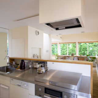 造作のキッチン。レンジフードも造作で囲い、見えないように。ガス台には蓋をつけ、普段は見えない。開くと油よけになる優れものだ。シンクの後ろは調味料を保管できるスペースで、その右側はリビング側から収納できるスペース。目隠しの壁ではなく、収納にした点がポイントだ
撮影：NewHouse出版