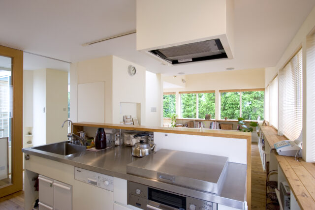 造作のキッチン。レンジフードも造作で囲い、見えないように。ガス台には蓋をつけ、普段は見えない。開くと油よけになる優れものだ。シンクの後ろは調味料を保管できるスペースで、その右側はリビング側から収納できるスペース。目隠しの壁ではなく、収納にした点がポイントだ
撮影：NewHouse出版